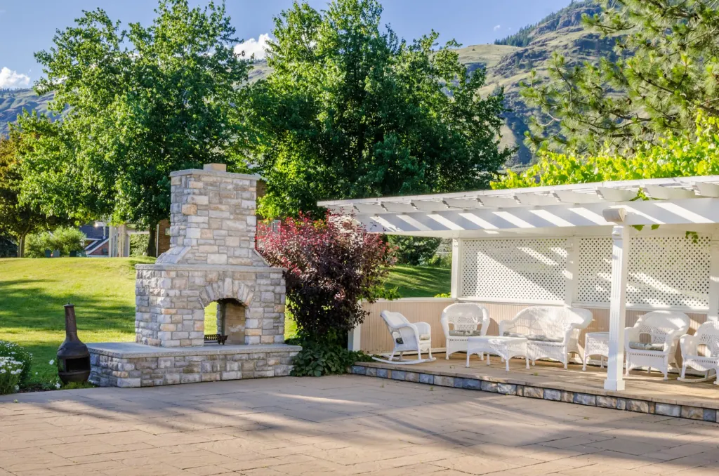 Paver patio under a white pergola with an outdoor fireplace