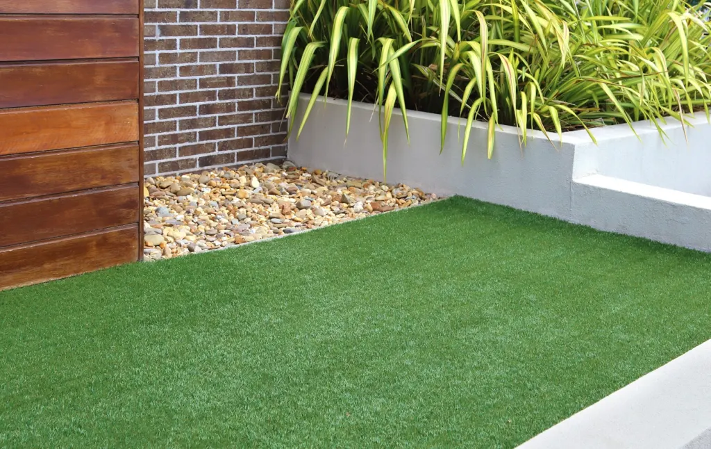 Artificial turf strip against a slat-wood wall and pebble drainage