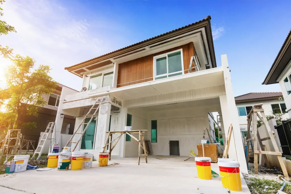 House exterior mid-repaint with ladders, buckets, and drop cloths